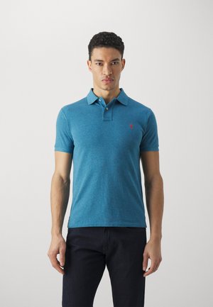 Polo shirt bleu en tissu tricot doux avec une patte de boutonnage à deux boutons, des manches courtes et un petit logo rouge sur la poitrine gauche.