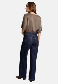 Top in maglia bronzo con vestibilità morbida, abbinato a jeans a gamba larga blu scuro con tasche posteriori e una cintura con stampa leopardata.