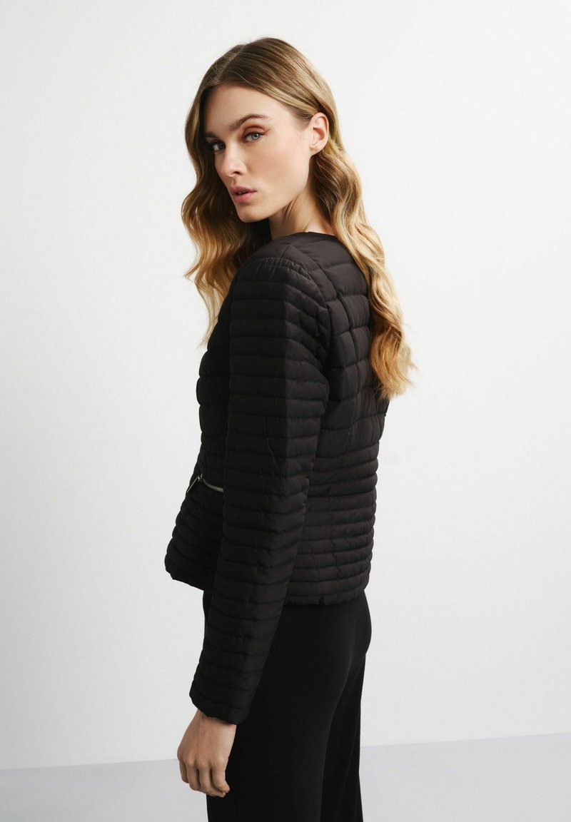 Schwarze, gesteppte Jacke mit Rundhalsausschnitt, langen Ärmeln und dezenten Reißverschlusseinzelheiten. Glatte Textur und cropped Design.