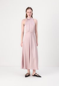 Rosa halterneckklänning med figursydd överdel, flödande kjol och textil med struktur; bärs med svarta flatskor med en dekorativ rosett.