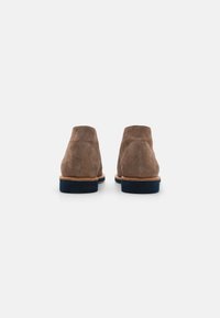 Stivaletti in suede marrone con una texture liscia, suole in gomma blu navy a contrasto e dettagli cuciti lungo il bordo superiore.