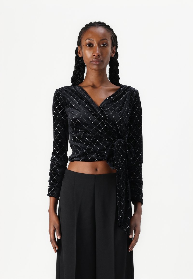 Μαύρη βελούδινη μπλούζα με μακριά μανίκια, με διαγώνιο μοτίβο από ασημένια διαμάντια και με κόμπο μπροστά. Συνδυάζεται με παντελόνι με φαρδιές γάμπες.