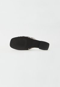 Sicht von unten auf einen schwarzen Schuh mit Absatz, der über eine strukturierte Sohle verfügt und ein Obermaterial mit Schlangenledermuster aufweist.