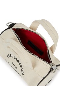 Krém színű vászon táska fekete kiegészítőkkel, piros belsővel, felső cipzárral és dupla hordozófüllel. Az elején logó található.