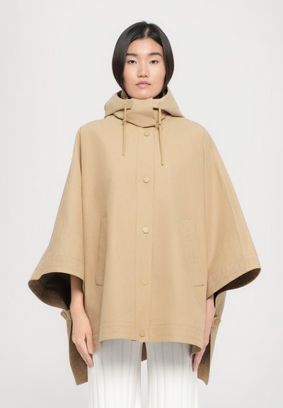 Beige Kapuzenponcho aus einem weichen, strukturierten Stoff mit goldenen Druckknöpfen, seitlichen Taschen und weiten Ärmeln.