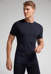 Námořnická modrá krátká rukávová tričko z hladkého materiálu, s kulatým výstřihem a přiléhavým střihem, nošené stojícím modelem.