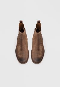 Botas de tobillo de ante marrón con una textura suave, puntera redondeada y cremalleras laterales, que cuentan con una suela de goma y lengüetas para un fácil uso.