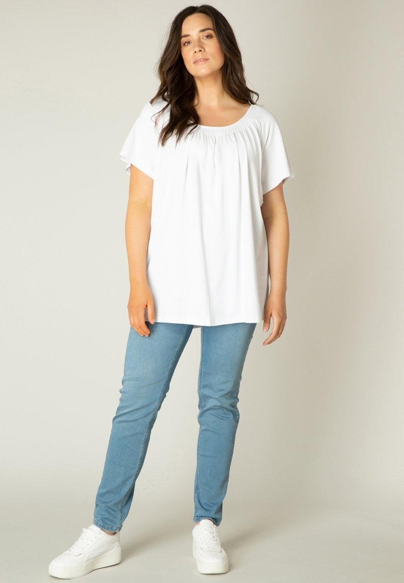 Witte korte mouw top met een geraffineerde halslijn, gecombineerd met lichtblauwe denim skinny jeans en witte platform sneakers.