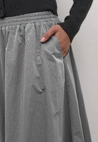 Grijze zijde rok met een elastische tailleband en zijzakken, met een gladde textuur en een vloeiende vorm, gedeeltelijk getoond met een hand in de zak.