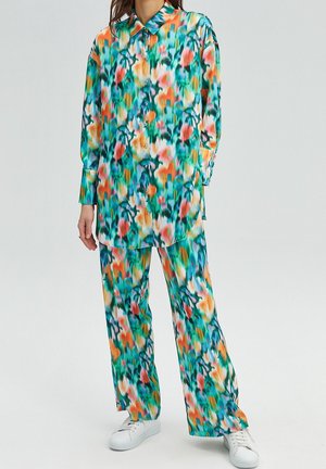 Woman wearing colorful floral print button-up long-sleeve shirt and matching wide-leg pants with white sneakers.