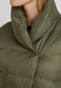 Chaqueta de plumas verde oliva con cuello alto, que presenta secciones acolchadas y un cierre delantero de botones. Textura suave y brillante.