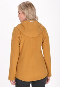 Mosterdgele softshell jas met capuchon, lange mouwen en een gebogen zoom. Voorzien van stikdetails en een label op de hals.