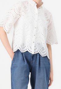 Witte broderie anglaise blouse met knopen, een gegolfde zoom en korte mouwen, met ingewikkelde uitsnijdingen en een relaxte pasvorm.
