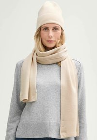 Beige ribbed knit beanie and scarf, soft texture, layered over a light grey sweater, showcasing a simple, classic design.
