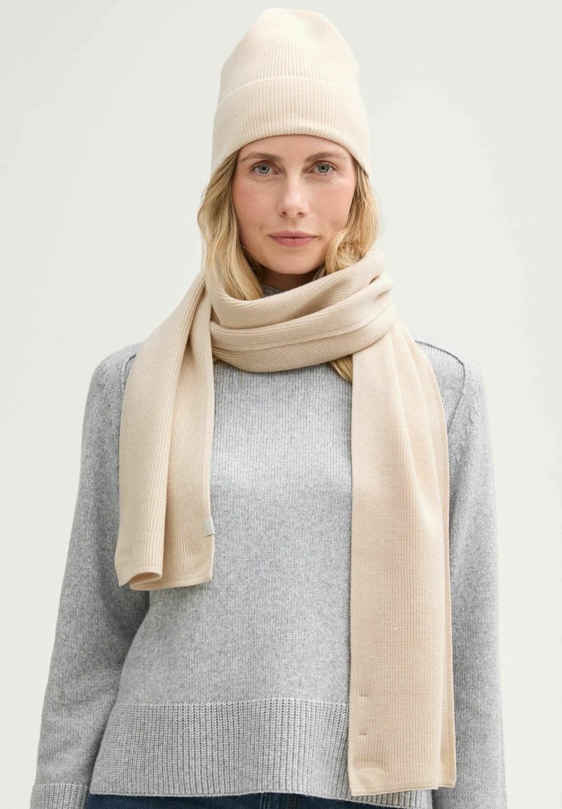 Beige ribbed knit beanie and scarf, soft texture, layered over a light grey sweater, showcasing a simple, classic design.
