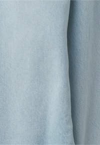 Tissu en denim bleu clair avec texture visible de tissage diagonal et légères plis naturels.