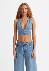 Denim krekls ar dziļu V veida kakla izgriezumu un divām priekšējām pogām. Modelis valkā platām kājām denim bikses ar aukliņu viduklī. Gaiši zilā krāsā.
