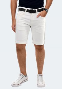White denim shorts with rolled cuffs, worn with a black belt. Paired with white sneakers featuring gray accents. Smooth texture.