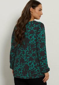 Langsleeve shirt in donkergroen met een zwart abstract bloemenpatroon, met een ronde halslijn en licht gegatherde mouwen.