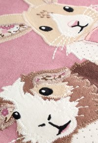 Tessuto ricamato con un coniglio e una pecora su sfondo rosa. I dettagli includono texture varie e motivi cuciti in colori tenui.