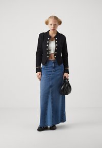 Veste militaire noire coupée avec des boutons dorés ; haut crop blanc froncé ; jupe en jean longue ; sac à main noir ; chaussures noires.