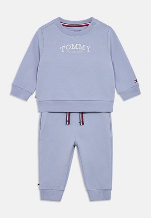 Šviesiai mėlynas Tommy Hilfiger kūdikių sportinis kostiumas su ilgomis rankovėmis, riboto audinio rankogaliais, logotipu ant krūtinės ir rankovės bei kelnėmis su raišteliais.