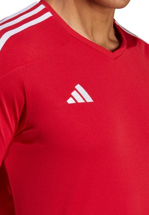 Rode sportieve jersey met V-hals en korte mouwen, met witte drie-strepen details op de schouders en een klein wit logo op de borst.