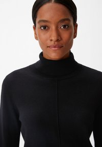 Schwarzer Rollkragenpullover aus weichem Strickstoff, mit einem strukturierten Design, langen Ärmeln und einer Nahtapplikation auf der Vorderseite.