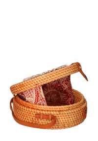 Cestino tondo intrecciato con finitura in rattan naturale e fodera in tessuto rosso a motivi, dotato di una tracolla in pelle e un bordo decorativo superiore.