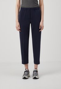 Pantalon à taille élastique marine avec une coupe ample, longueur raccourcie et revers roulés, associé à des chaussures de sport noires et argentées.
