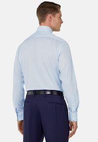 Camicia azzurra chiaro con maniche lunghe, colletto a punta e polsini abbottonati, abbinata a pantaloni scuri blu navy con tasche e una cintura nera.