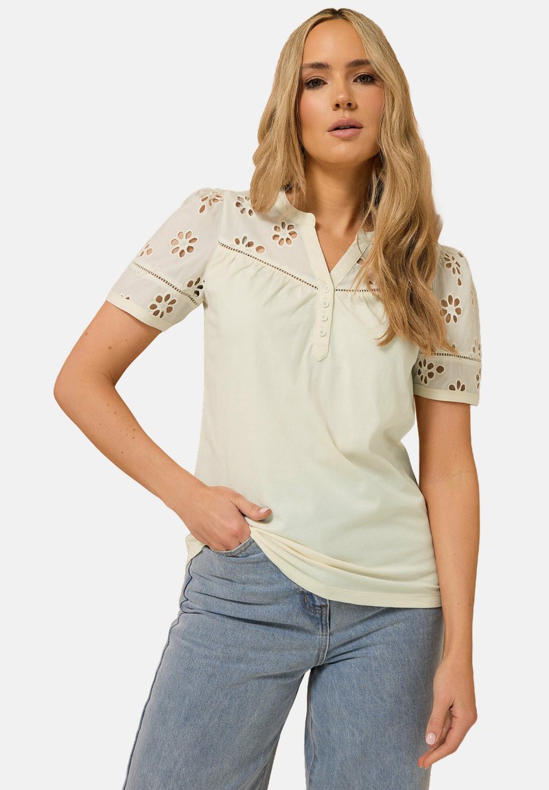 Light green cotton shirt with short sleeves, featuring floral cutout details and a buttoned placket. Paired with blue jeans.