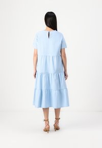 Vestido em azul claro com camadas, mangas curtas, decote redondo e detalhe em gota nas costas. Tecido macio com textura suave.