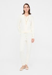 Set di abbigliamento loungewear color crema composto da una giacca con zip e colletto e pantaloni tapered coordinati, realizzati in un materiale morbido e testurizzato.