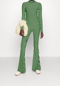 Długi rękaw zielono-czarna bluzka w paski i dzwony. Przezroczysta tekstura. Biała torebka z futrzanymi detalami. Buty z drewnianą podeszwą.