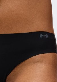 Κοντινό πλάνο στον γοφό ενός ατόμου που φοράει μαύρα μαγιό Under Armour με ένα μικρό λογότυπο στην πάνω πλευρά.