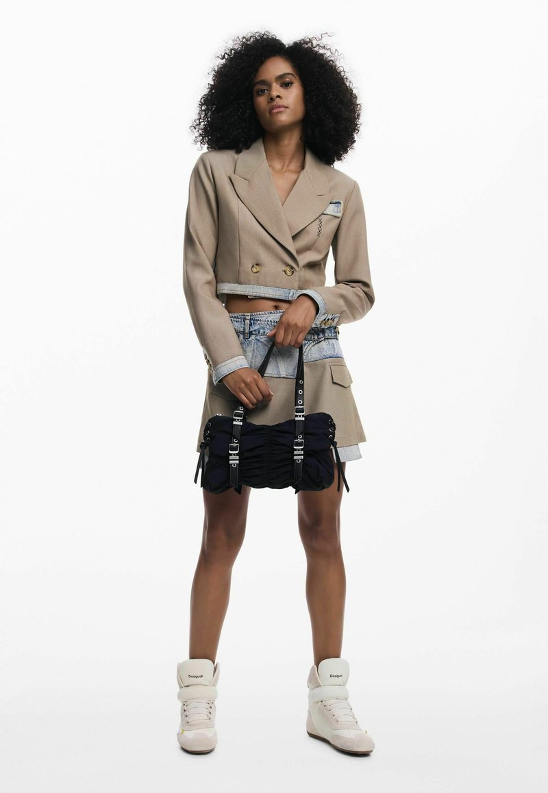 Blazer beige court à double boutonnage, mini-jupe en denim, sac à main bleu marine froncé avec ferrures argentées, et baskets montantes crème.