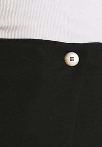 Black skirt featuring a textured fabric with a smooth finish; highlights a white button detail at the waistband.
