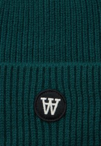 Tessuto a maglia a coste verde scuro con una toppa rotonda nera che presenta lettere AA ricamate in bianco.