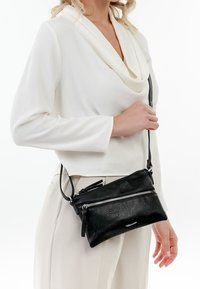 Borsa a tracolla in pelle nera con due scomparti con zip, texture liscia e tracolla regolabile, esposta su uno sfondo bianco.