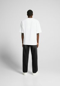 Maglietta bianca oversize con maniche corte, abbinata a pantaloni neri larghi e sneakers bianche. Design minimalista con una silhouette pulita.