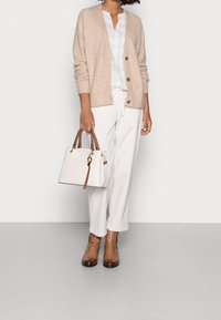 Beige neuleneuletakki napillisesti suljettuna, valkoinen paita, valkoiset nauhakiiltoiset housut, ruskeat nilkkurit ja valkoinen käsilaukku ruskeilla yksityiskohdilla.