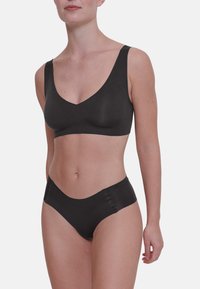 Bralette nera senza cuciture con spalline larghe e scollatura a V profonda. Abbinata a slip bikini a vita media coordinati. Texture liscia.
