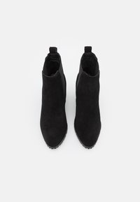 Bottines en suede noir avec un extérieur lisse, un bout rond, des panneaux latéraux élastiques et une semelle en caoutchouc texturée. Pas de matériel ou de motifs visibles.