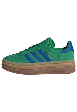 Zielony zamszowy sneaker Adidas Gazelle z niebieskimi paskami i piętą, podeszwą z gumy warstwowej oraz tłoczonym logo po bokach i na podeszwie.