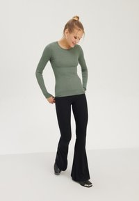 Rippenshirt mit langen Ärmeln in Grün, kombiniert mit schwarzen, enganliegenden Schlagleggings. Das Shirt hat einen runden Halsausschnitt und einen strukturierten Stoff.