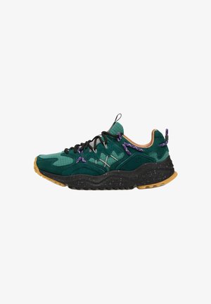 Sneaker verde e nero con suola testurizzata, lacci neri e viola e rivestimento interno beige, mostrato in profilo laterale su sfondo bianco.