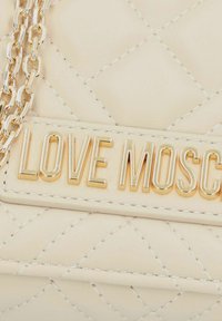 Borsa a tracolla cremosa trapuntata con catena dorata e placca con logo "LOVE MOSCHINO" in oro, caratterizzata da una texture liscia e dettagli cuciti.