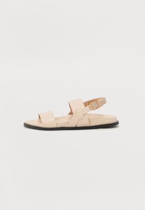 Beige leren sandaal met twee brede banden over de voet en een verstelbare enkelband, met een zwarte rubberen zool en een minimalistisch design.