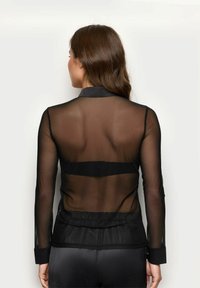 Schwarzes, durchscheinendes Langarmshirt mit Kragen, elastischem Bund und einfarbigen schwarzen Manschetten. Hat einen durchsichtigen Rücken.